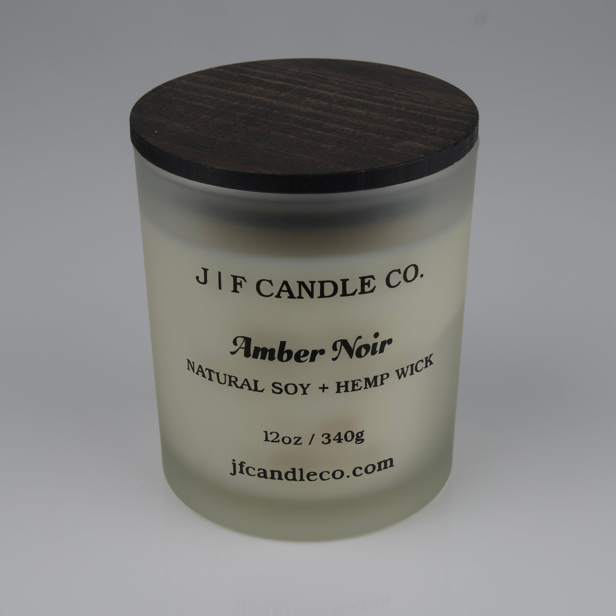 Frosted candle jar with brown lid labeled JF Candle Co. Amber Noir on a white background