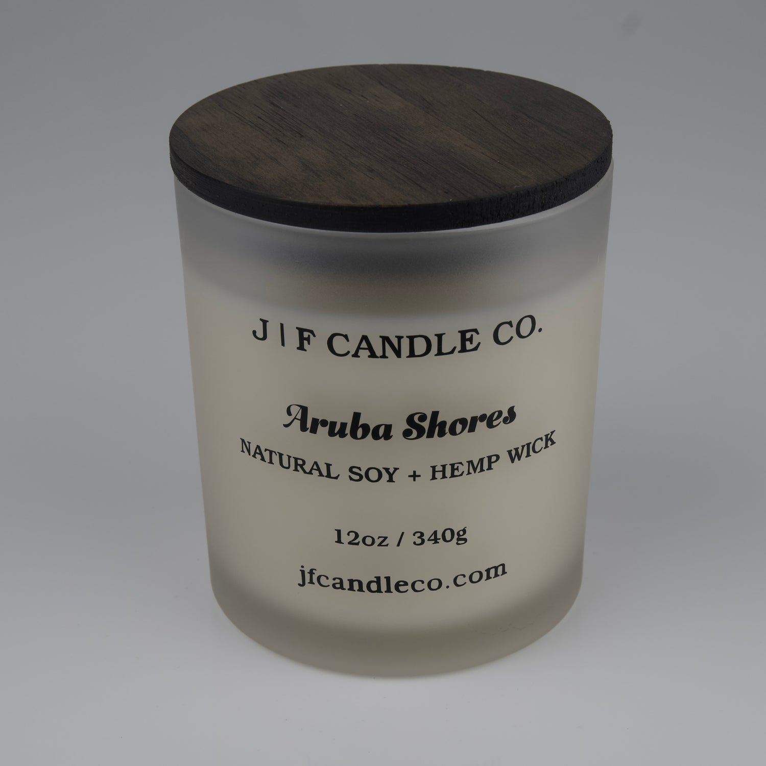 Frosted candle jar with wooden lid labeled 'J/F Candle Co. Aruba Shores'