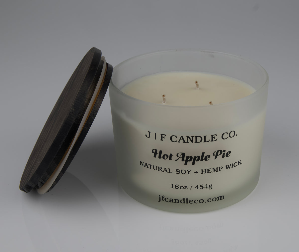 Hot Apple Pie Soy Candle by JF Candle Co. in a frosted glass jar with wooden lid resting on side of jar, 16oz hand-poured natural soy wax with hemp wick.