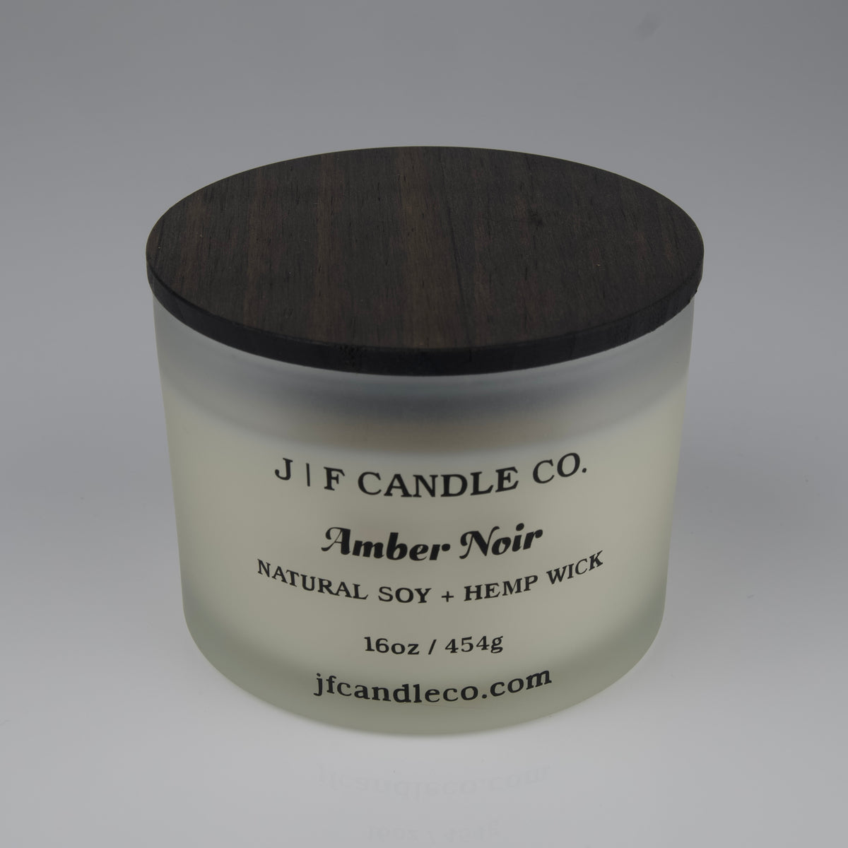Frosted candle jar with wooden lid labeled 'J|F Candle Co. Amber Noir' on a white background