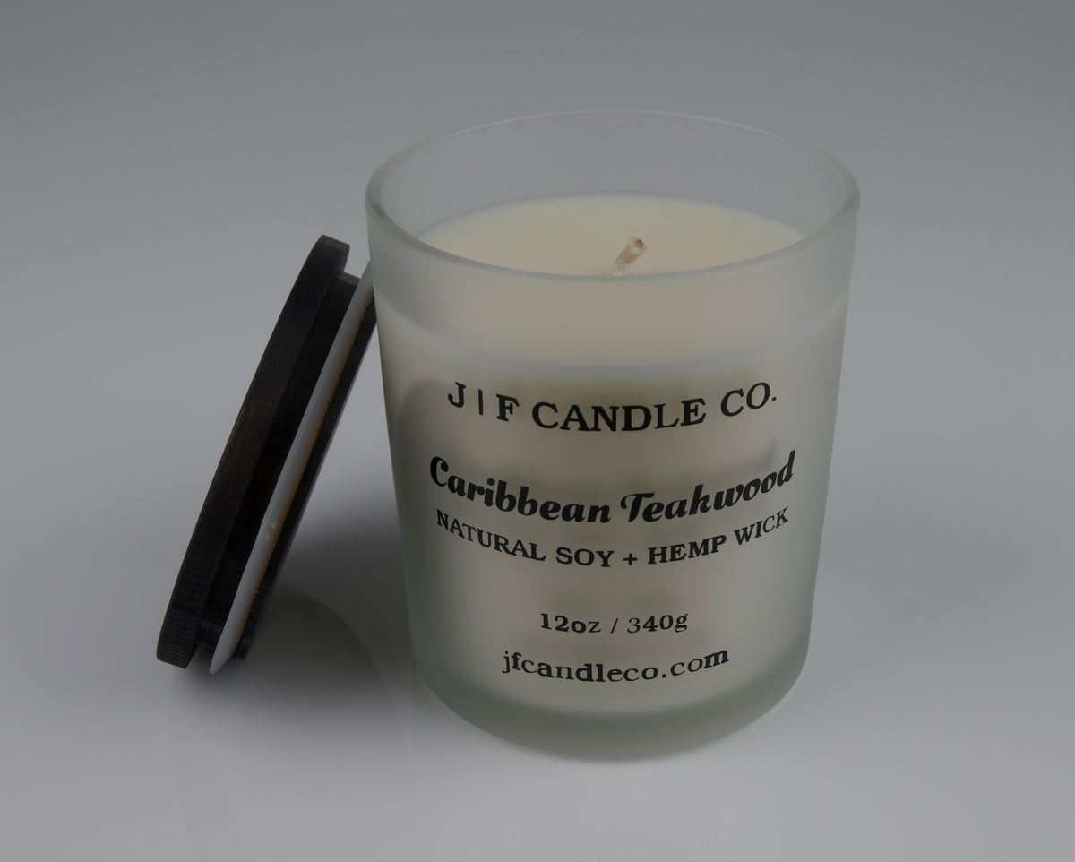 Frosted glass candle with wooden lid labeled 'J|F Candle Co. Caribbean Teakwood' with lid rested on side of jar