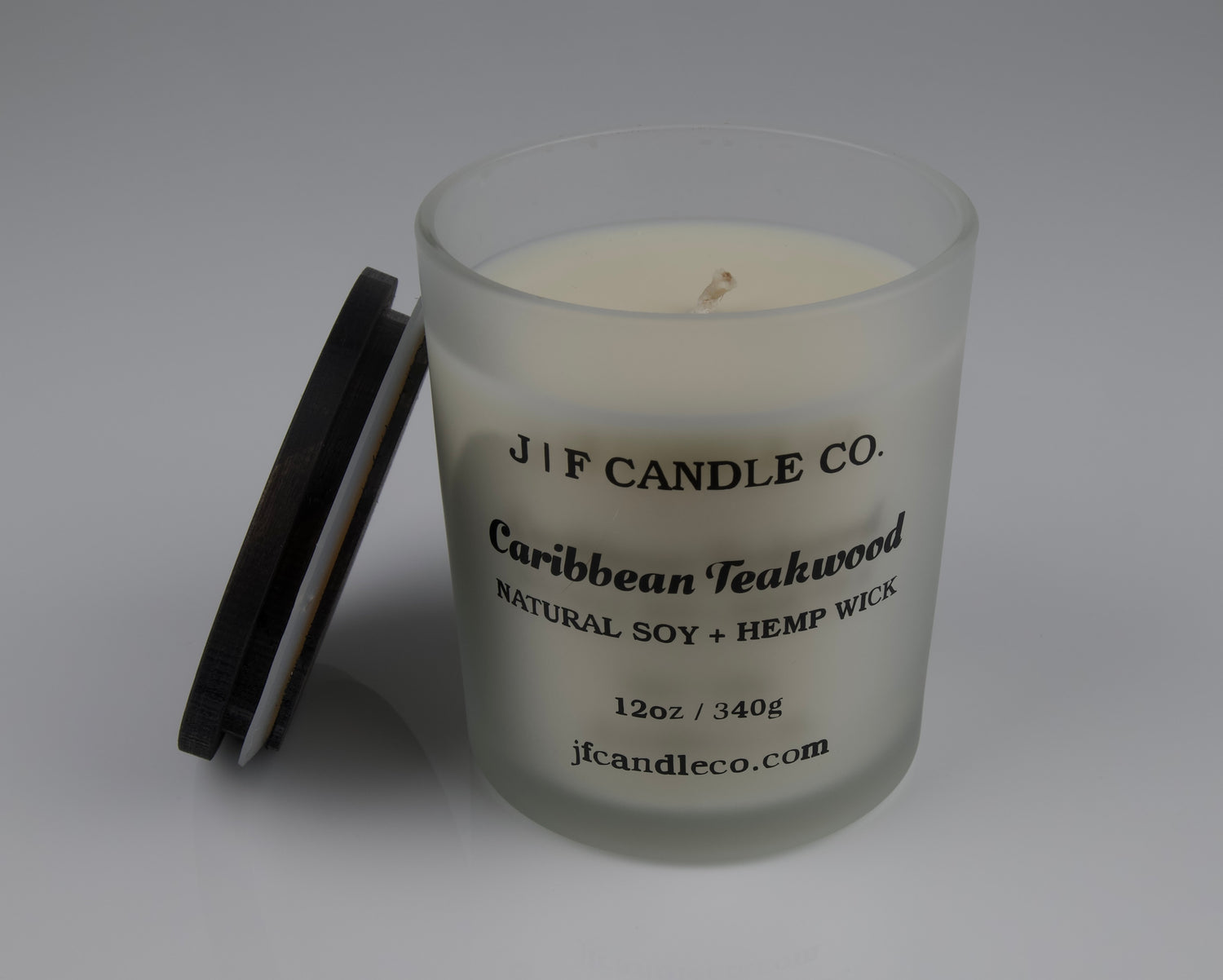 Frosted glass candle with wooden lid labeled 'J|F Candle Co. Caribbean Teakwood' with lid rested on side of jar