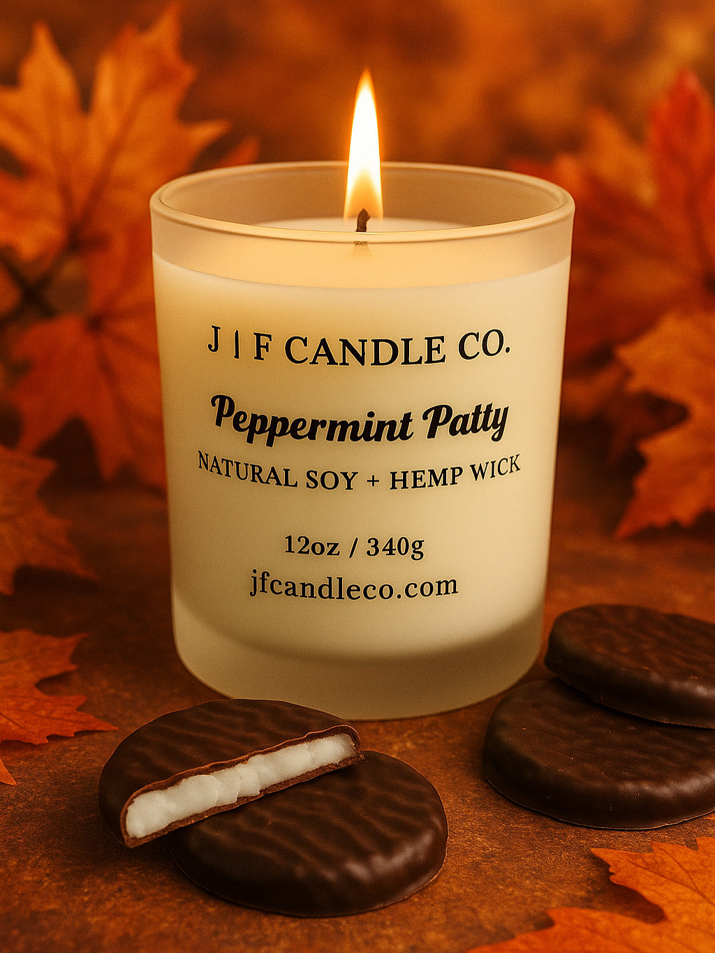 A lit “Peppermint Patty” candle by J | F Candle Co., crafted with natural soy and a hemp wick, sits on a warm autumn backdrop surrounded by chocolate mint cookies and scattered fall leaves, evoking a cozy seasonal atmosphere.