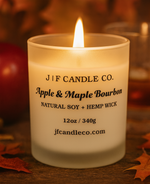 A lit Apple & Maple Bourbon soy candle by J | F Candle Co. in a frosted glass jar with the lid removed, styled in an autumn setting with apple slices and bourbon-themed props, showcasing a soft flame and original product label.