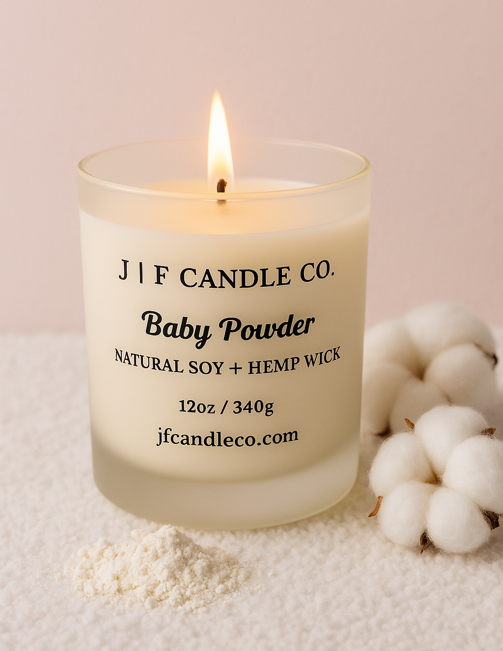 Baby Powder scented soy candle in a frosted glass jar with a lit wick, cotton accents, and a small sprinkle of powder in front.