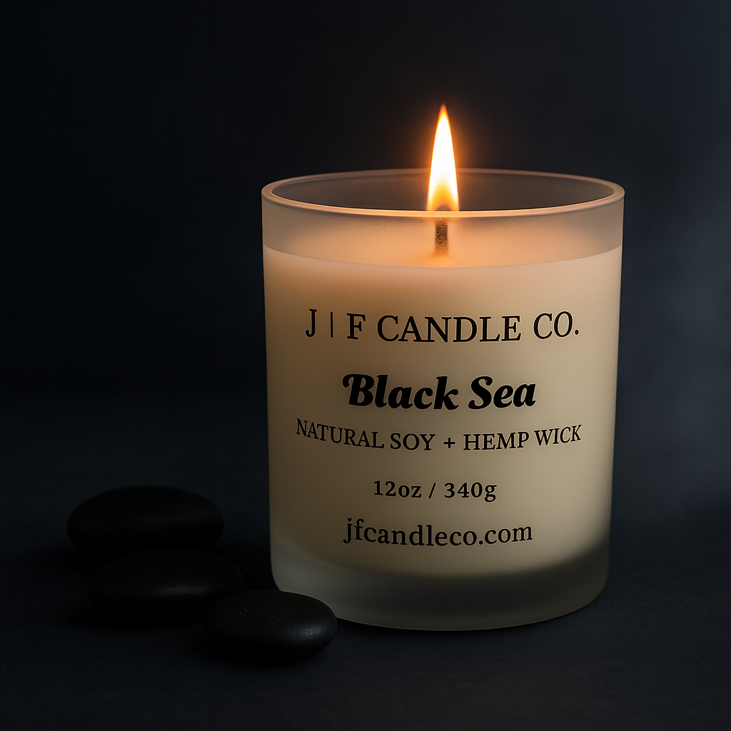 Black Sea soy candle by J | F Candle Co., photographed with a soft coastal haze and modern black river stones for a clean upscale spa aesthetic.
