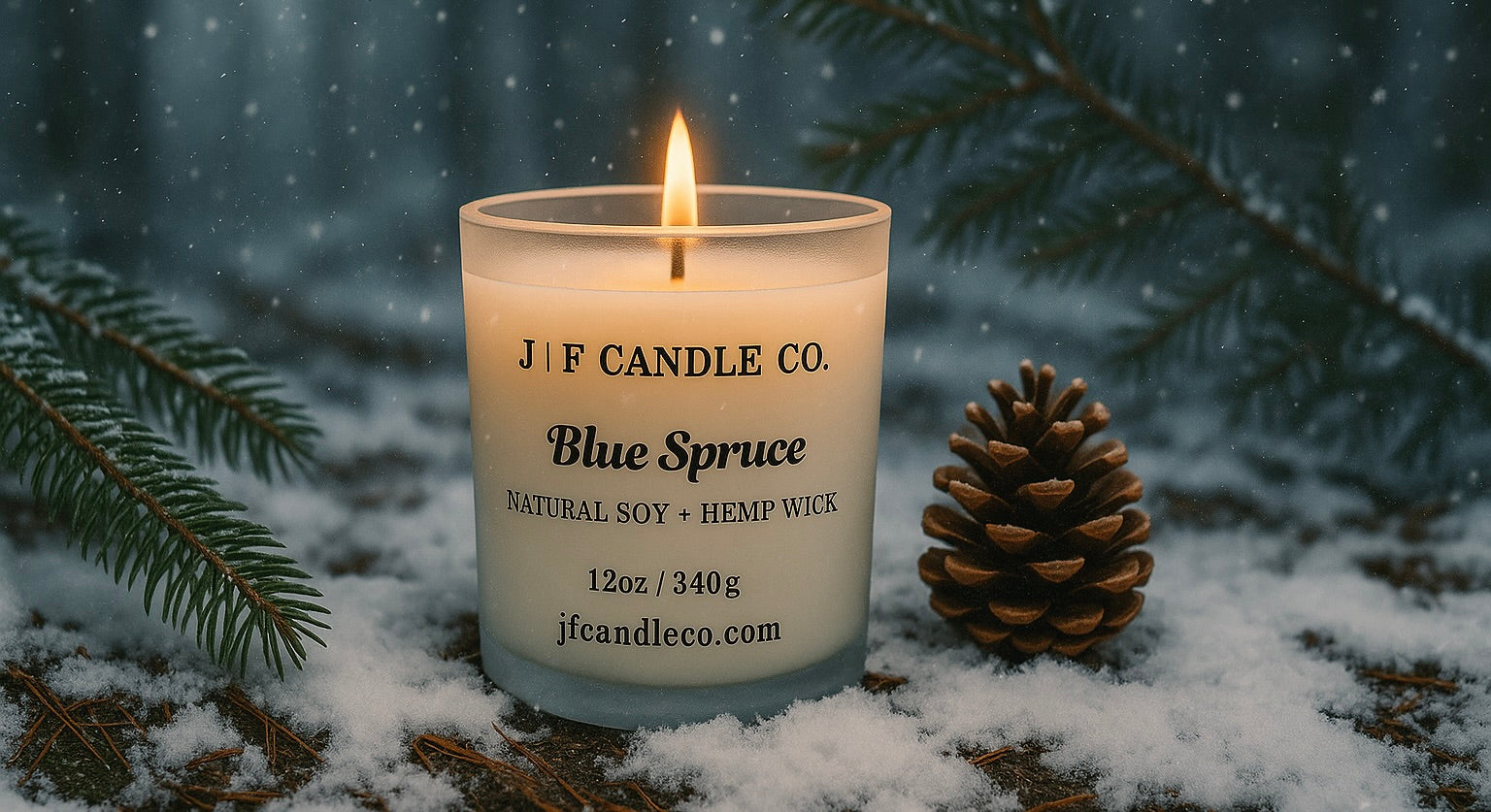 J | F Candle Co. Blue Spruce soy candle lit in a snowy forest setting with pine needles, branches, and pinecone — frosted glass jar with hemp wick glowing warmly amid winter snowfall.