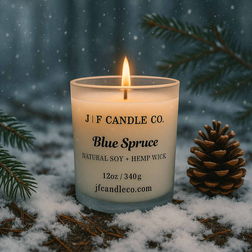 Blue Spruce scented soy candle by J | F Candle Co. burning outdoors in the snow, surrounded by pine branches and a pine cone, creating a cozy winter forest atmosphere.
