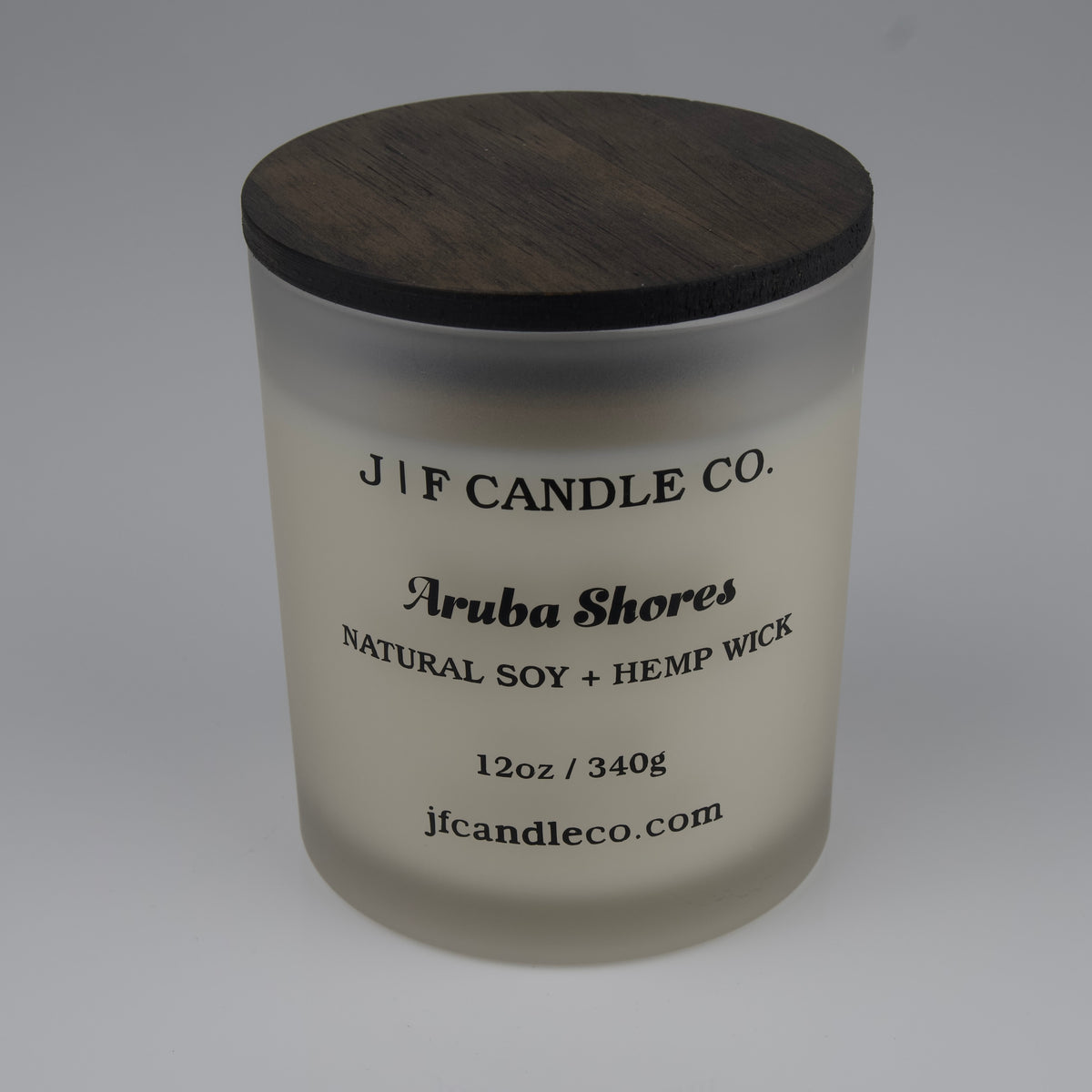 Frosted candle jar with wooden lid labeled 'J/F Candle Co. Aruba Shores'