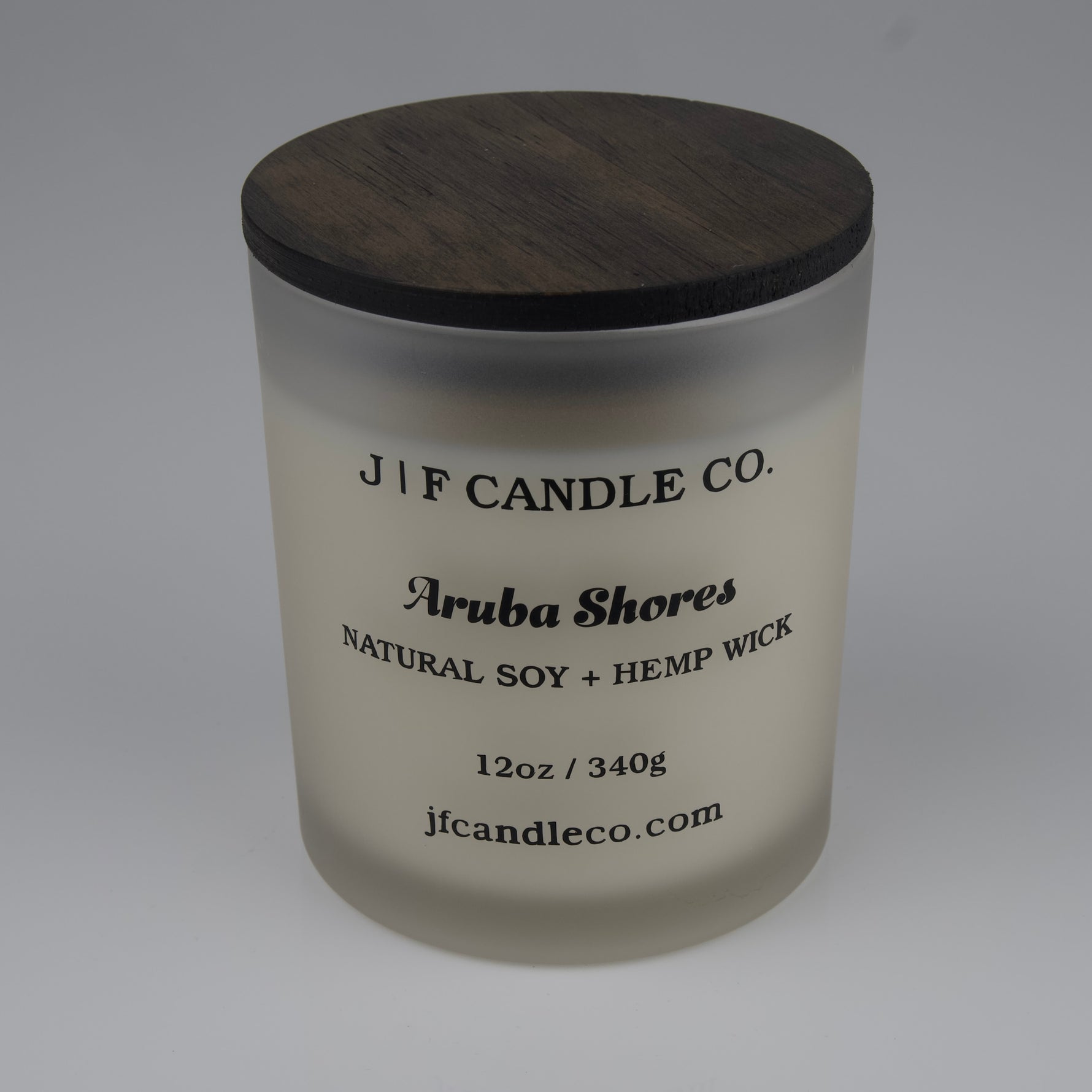 Frosted candle jar with wooden lid labeled 'J/F Candle Co. Aruba Shores'