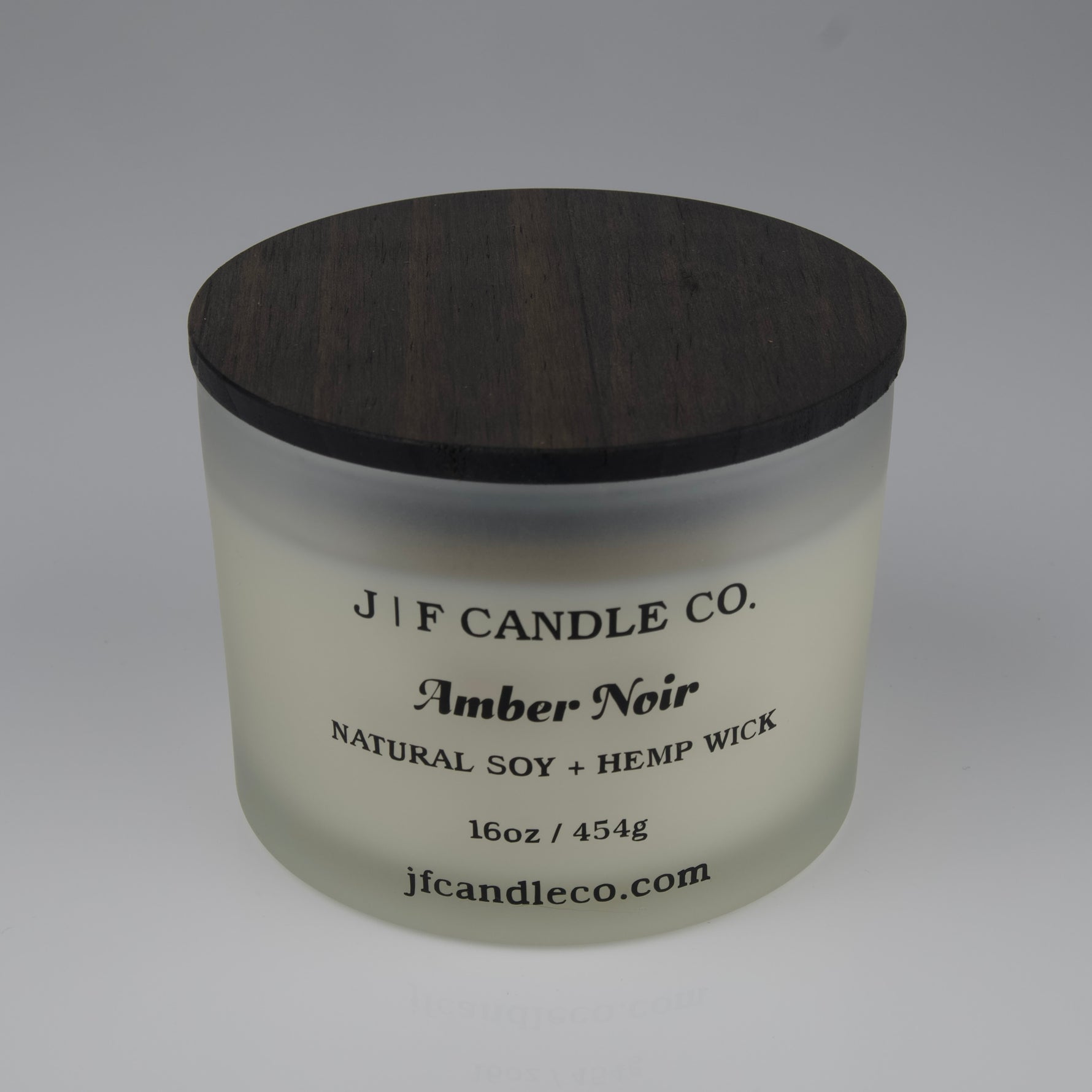 Frosted candle jar with wooden lid labeled 'J|F Candle Co. Amber Noir' on a white background