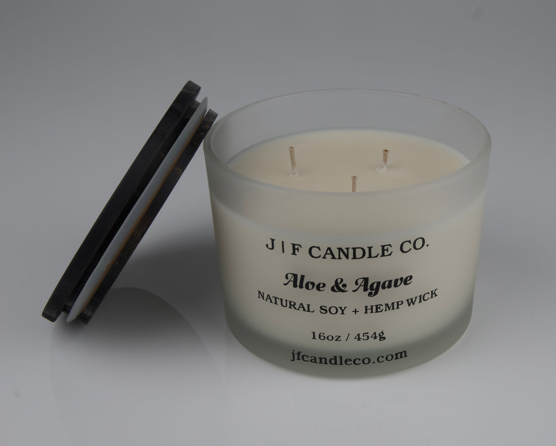 JF Candle Co. 16oz Aloe and Agave soy candle with 3 hemp wicks in frosted glass jar, dark wooden lid resting beside it.