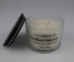 16oz Frosted glass candle with wooden lid labeled 'J|F Candle Co. Caribbean Teakwood' with lid rested on side of jar