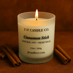 A lit Cinnamon Stick candle by J | F Candle Co. in a frosted glass jar, surrounded by cinnamon sticks on a warm brown background.