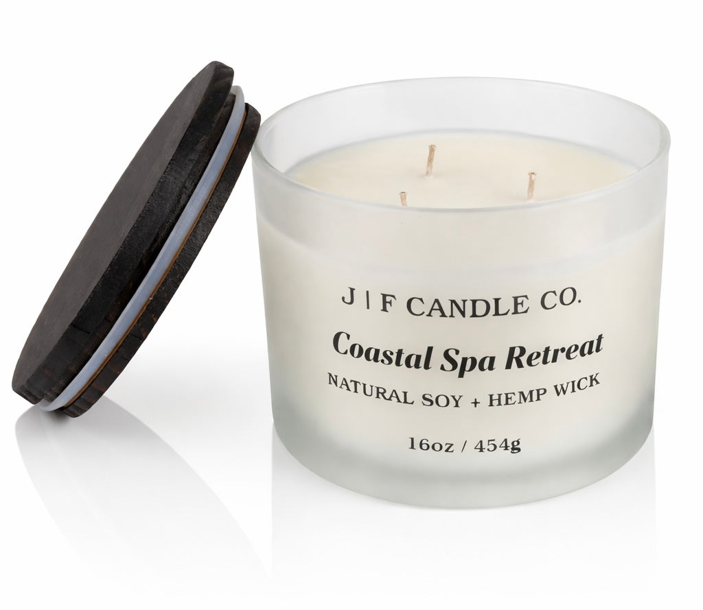 16oz Coastal Spa Retreat soy candle by J | F Candle Co. with three wicks in a frosted glass jar, wooden lid placed beside it on a clean white background.