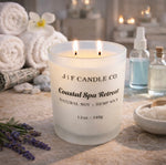 Double wick Coastal Spa Retreat candle by J | F Candle Co. lit on a stone surface in a serene spa setting, styled with rolled towels, lavender, bath salts, and glass apothecary bottles for a calm, luxury atmosphere.