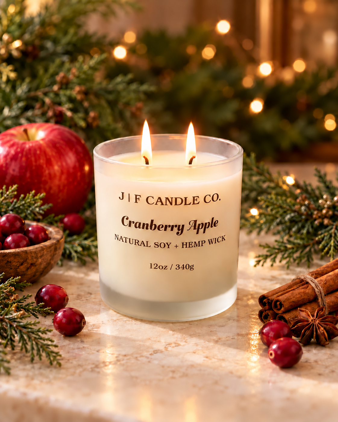 Lit Cranberry Apple soy candle with evergreen branches, cranberries, and warm holiday lights