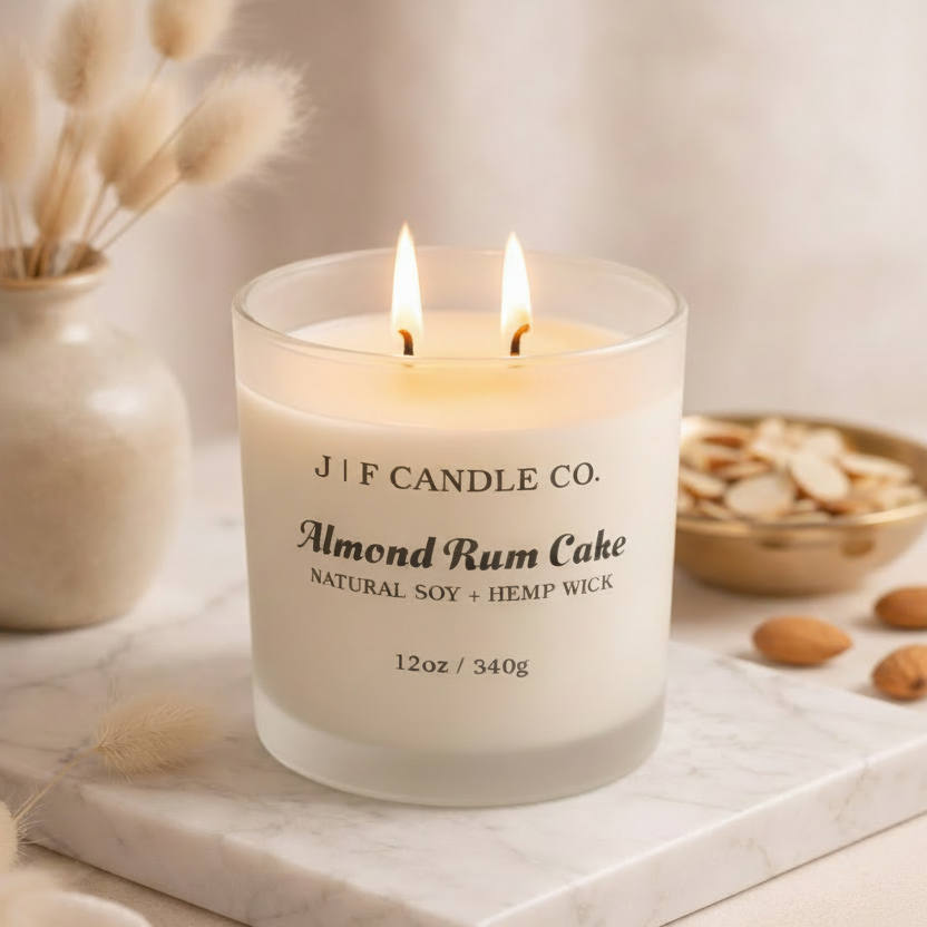 J | F Candle Co. Almond Rum Cake 12 oz natural soy candle lit on marble surface with almonds and warm luxury styling