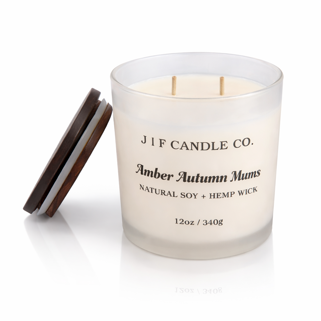 J | F Candle Co. Amber Autumn Mums luxury soy candle in a frosted glass 12 oz jar with double unlit hemp wicks, black label, wooden lid beside jar, and soft reflection on a clean white background.