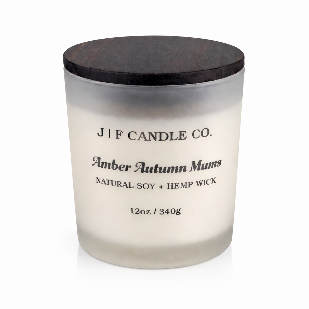 J | F Candle Co. Amber Autumn Mums 12 oz luxury soy candle in a frosted glass jar with dark wooden lid, black label, and soft reflection on a clean white background.