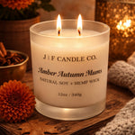J | F Candle Co Amber Autumn Mums luxury soy candle with double wick burning in a warm fall lifestyle setting with orange chrysanthemums, oak leaves, and cozy ambient lighting