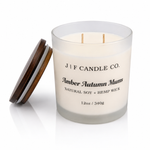 J | F Candle Co. Amber Autumn Mums luxury soy candle in a frosted glass 12 oz jar with double unlit hemp wicks, black label, wooden lid beside jar, and soft reflection on a clean white background.