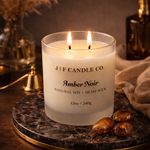 Amber Noir luxury soy candle by J | F Candle Co., 12 oz frosted glass jar with double hemp wicks, clean-burning natural soy wax, warm amber scented candle on marble tray with cozy lifestyle setting.