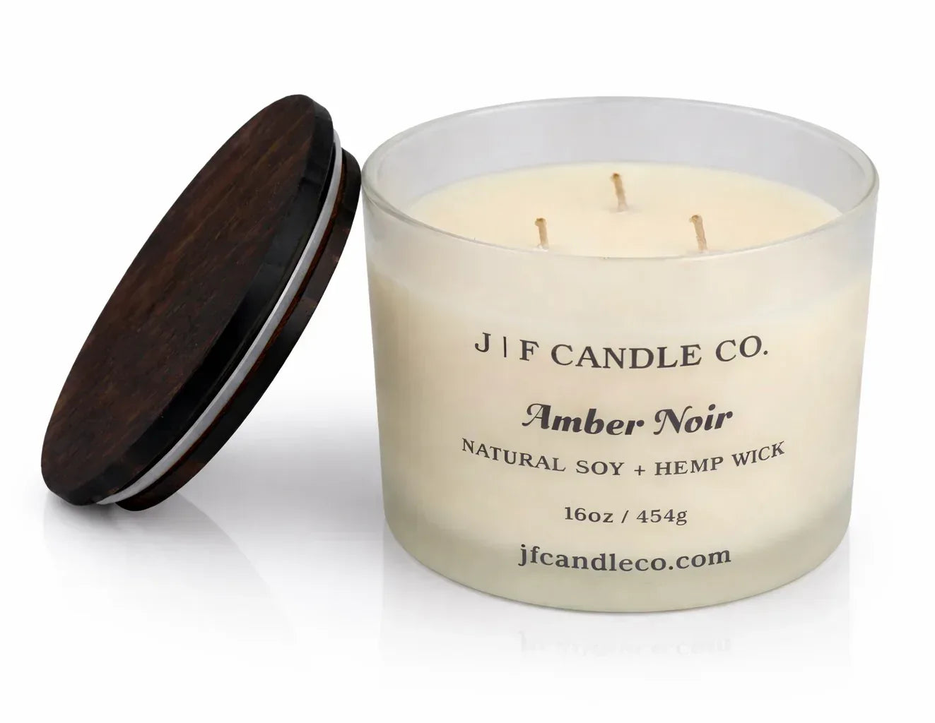 Amber Noir luxury soy candle in a frosted glass jar with wooden lid beside it, featuring three wicks and a soft reflective surface on a clean white background.