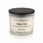 Luxury frosted glass soy candle with dark wooden lid labeled “Amber Noir,” softly illuminated on a clean white background with a subtle reflection beneath the jar.