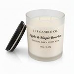 J | F Candle Co. Apple & Maple Bourbon soy candle in a frosted glass jar with wooden lid beside it, clean studio background with soft reflective surface.