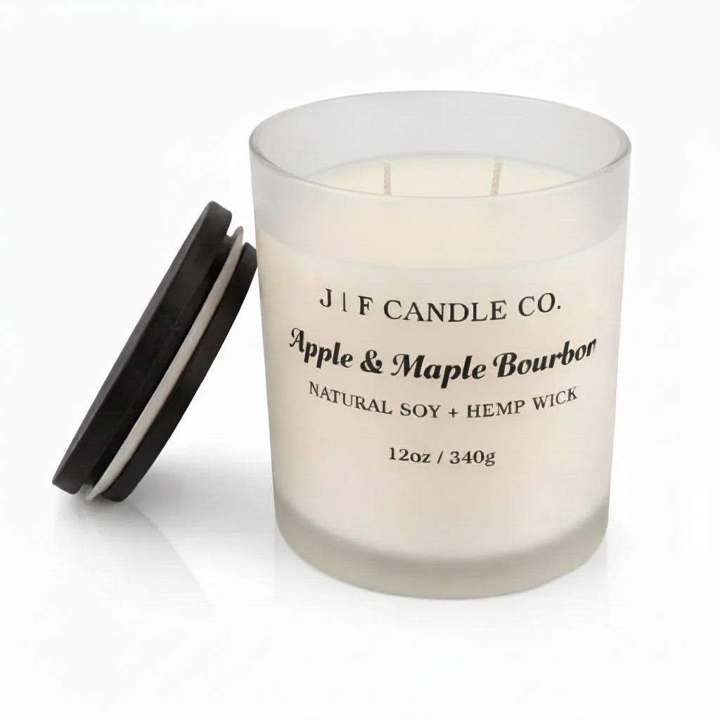 J | F Candle Co. Apple & Maple Bourbon soy candle in a frosted glass jar with wooden lid beside it, clean studio background with soft reflective surface.
