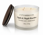 Luxury frosted glass J | F Candle Co. Apple & Maple Bourbon 16oz soy candle with wooden lid resting beside jar and a soft reflective surface beneath.