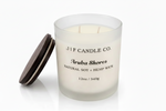 J | F Candle Co. Aruba Shores 12oz soy candle in a frosted glass jar with wooden lid resting beside it, shown on a clean white background with a soft reflection beneath the candle.