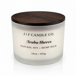 Luxury frosted glass Aruba Shores soy candle with wooden lid, soft reflection beneath jar, clean white background.