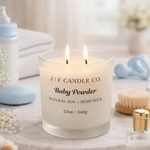 J | F Candle Co. Baby Powder luxury soy candle in a frosted 12 oz glass jar with two lit hemp wicks, styled on a marble tray with soft baby essentials, delicate florals, and gold accents in a light, airy setting.