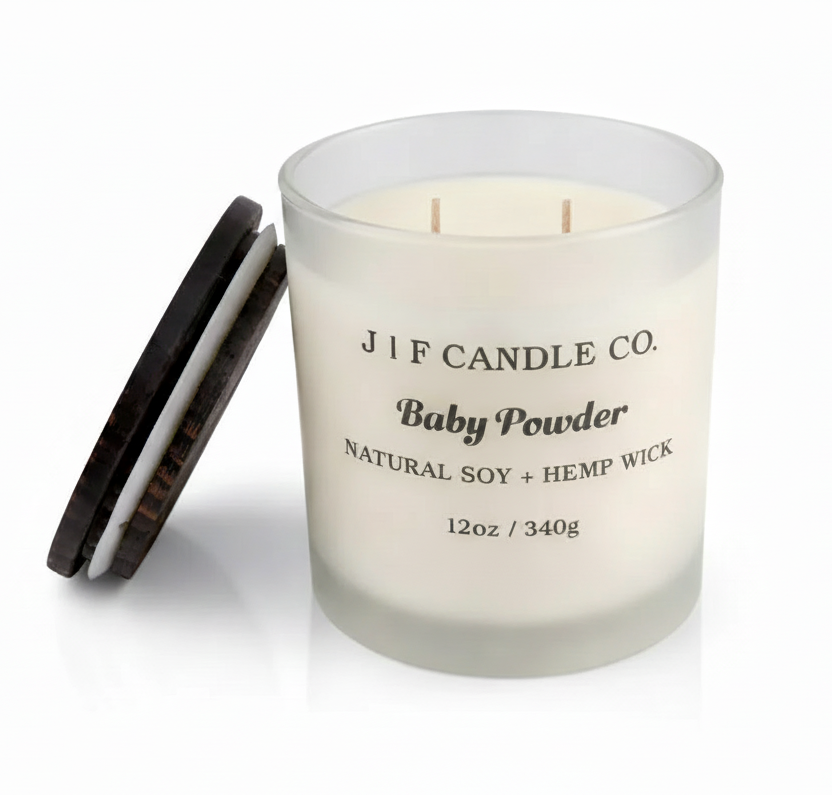J | F Candle Co. Baby Powder 12oz soy candle in frosted glass jar with wooden lid beside candle and soft reflection on a clean white background.