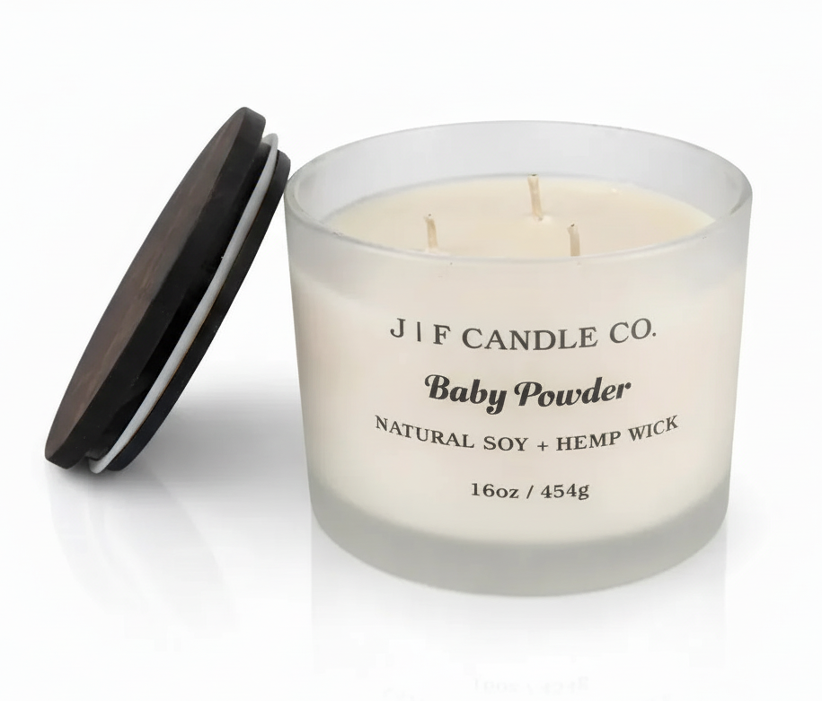 J | F Candle Co. Baby Powder 16oz three-wick soy candle in frosted glass jar with wooden lid beside candle and soft reflection on a clean white background.