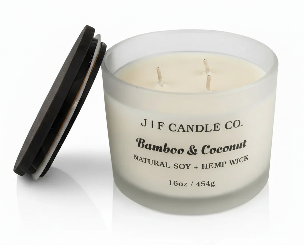 J F Candle Co Bamboo & Coconut 16 oz soy candle with three wicks in a frosted glass jar with wooden lid beside it on a clean white background with soft reflection