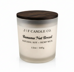 J F Candle Co Banana Nut Bread 12 oz soy candle in a frosted glass jar with wooden lid on a clean white background with soft reflection