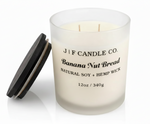 J F Candle Co Banana Nut Bread 12 oz soy candle in a frosted glass jar with wooden lid beside it on a clean white background with soft reflection