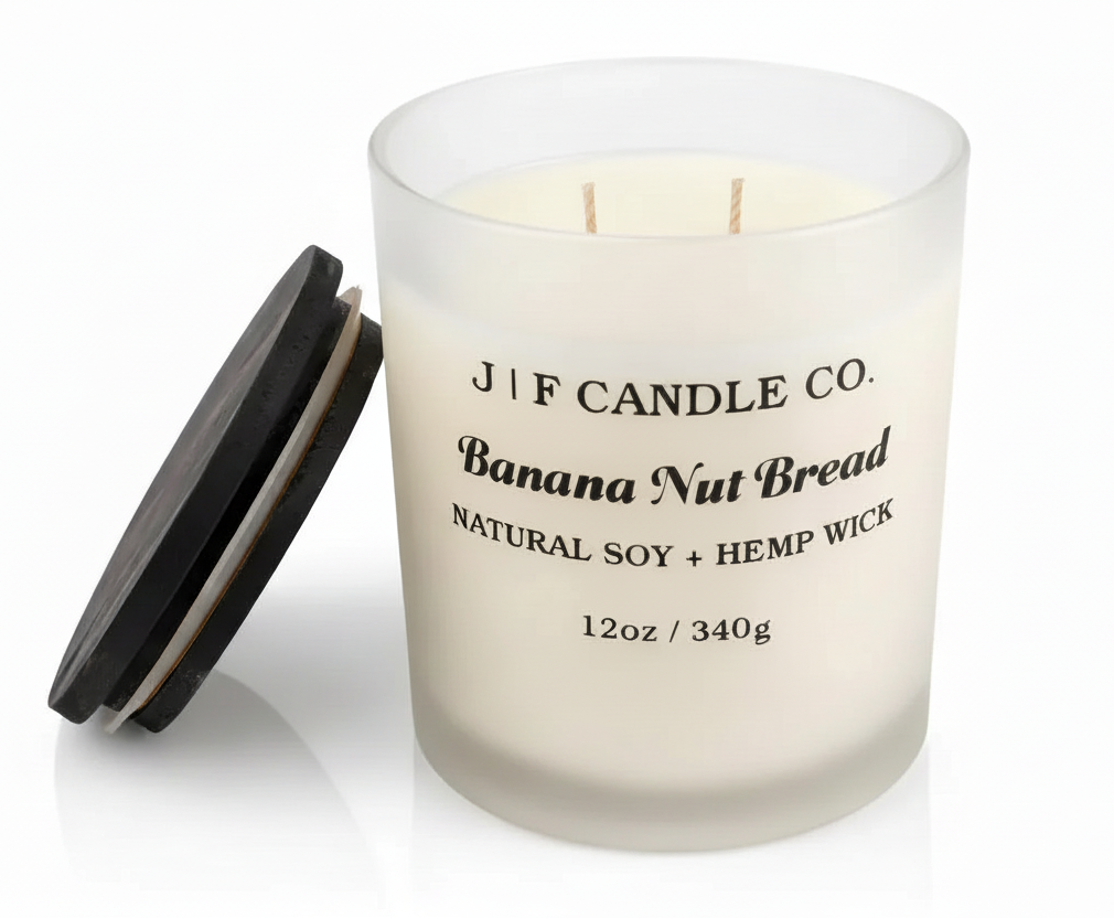 J F Candle Co Banana Nut Bread 12 oz soy candle in a frosted glass jar with wooden lid beside it on a clean white background with soft reflection