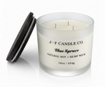 J | F Candle Co. Blue Spruce 16 oz natural soy candle in frosted glass jar with wooden lid beside candle
