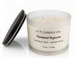 J | F Candle Co. Caramel Popcorn 16 oz natural soy candle with lid off showing triple wick in frosted glass jar and soft reflection on clean white background