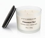 J | F Candle Co. Cinnamon Chai 16oz triple wick soy candle in a frosted glass jar with wooden lid placed beside it on a clean white background with a soft reflection.