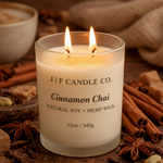 J | F Candle Co. Cinnamon Chai soy candle in a frosted glass jar with a lit wick, styled on a rustic wood surface surrounded by cinnamon sticks, star anise, and chai spices in a warm, cozy setting.