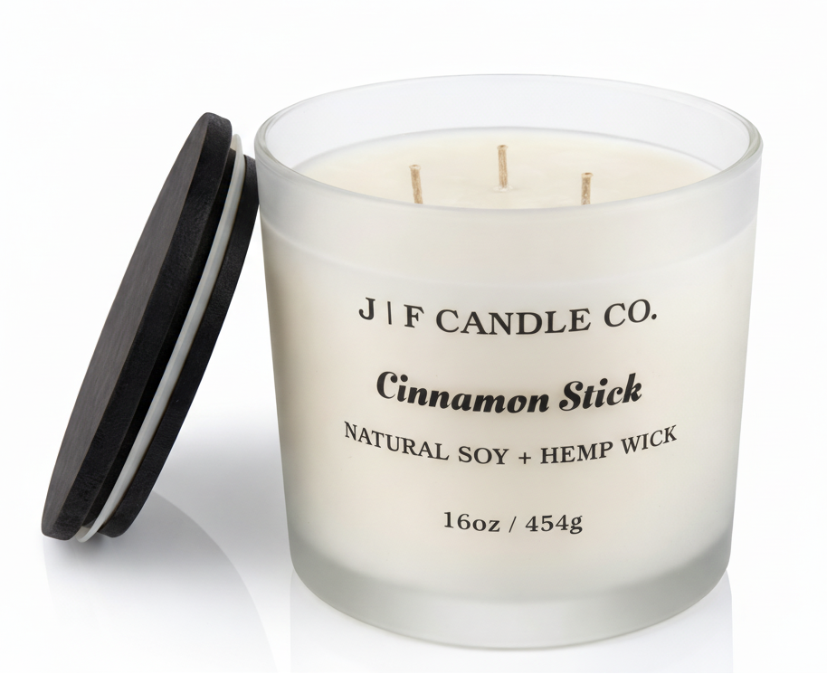 J | F Candle Co. Cinnamon Stick 16oz triple wick soy candle in frosted glass jar with wooden lid placed beside it on a clean white background with soft reflection