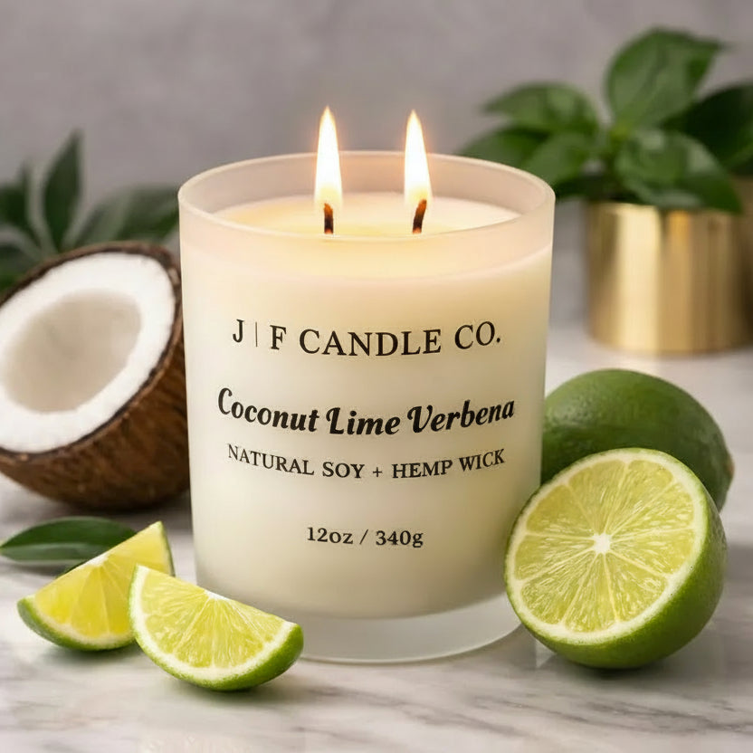 J | F Candle Co. Coconut Lime Verbena luxury soy candle in a frosted glass jar, lit wick, styled with fresh lime slices and coconut on a marble surface.