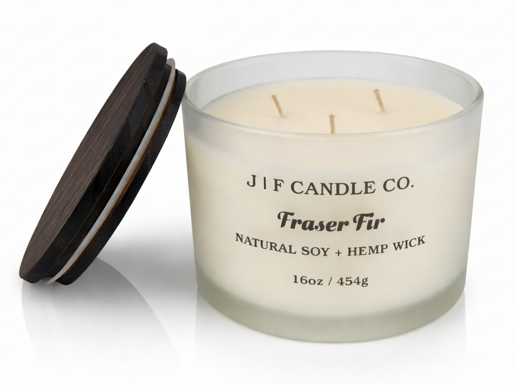 J | F Candle Co Fraser Fir 16oz three wick soy candle in frosted glass jar with wooden lid beside candle on white background with soft reflection