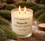 J | F Candle Co. Fraser Fir soy candle with a lit wick in a frosted glass jar, styled on a rustic wood surface with fresh evergreen branches, pinecones, and a soft winter ambiance