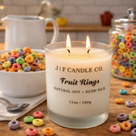 J | F Candle Co. Fruit Rings soy candle with a lit wick in a frosted glass jar, styled on a kitchen countertop with colorful fruit cereal, a bowl of cereal, and a glass jar of cereal in a warm, playful setting